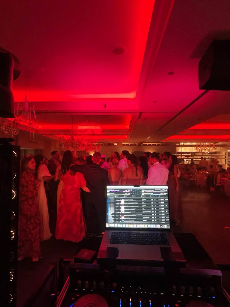 Invités qui dansent sous une lumière rouge, ordinateur du DJ au premier plan