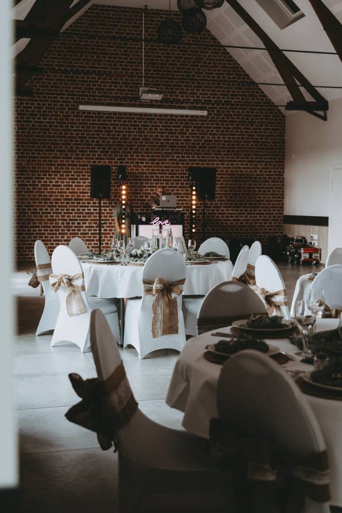 Salle de réception, tables rondes et néon love devant un mur de briques
