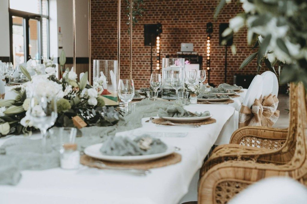 Table de mariage fleurie, chaises en rotin et stand DJ devant un mur de briques